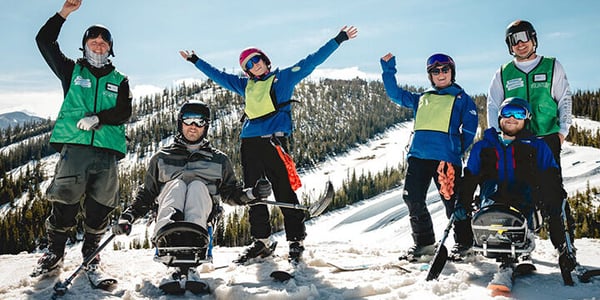 NSCD participants and volunteers on skis and adaptive skis cheering from a ski slope.