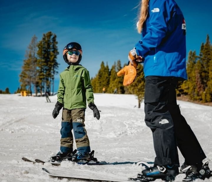 A young participant smiles during an adaptive ski lesson with an NSCD instructor on a sunny mountain slope.