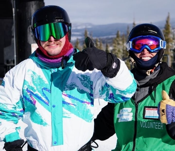 An NSCD participant and volunteer smile and give thumbs-up while standing together on the mountain