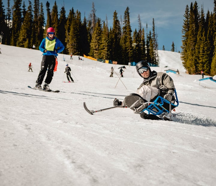 Sit ski participant getting an individual lesson from an NSCD volunteer.