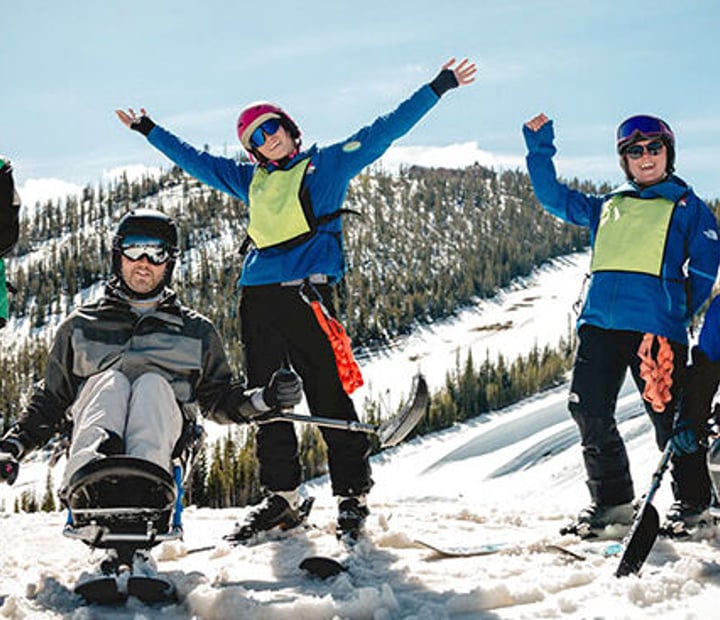 NSCD participants and volunteers on skis and adaptive skis cheering from a ski slope.