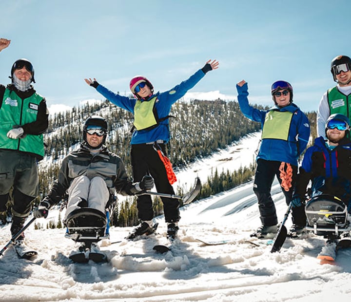 NSCD participants and volunteers on skis and adaptive skis cheering from a ski slope.