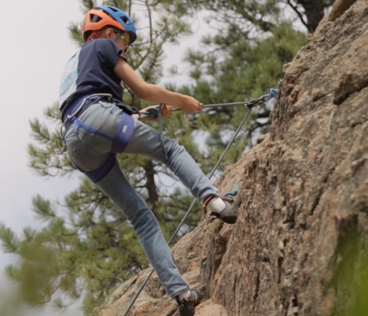 Close up of a young climber at the top of his outdoor climbing route, getting ready to slowly come down from his climb.