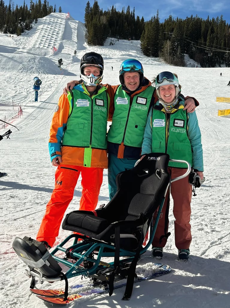 Two volunteers helping an adaptive ski athlete