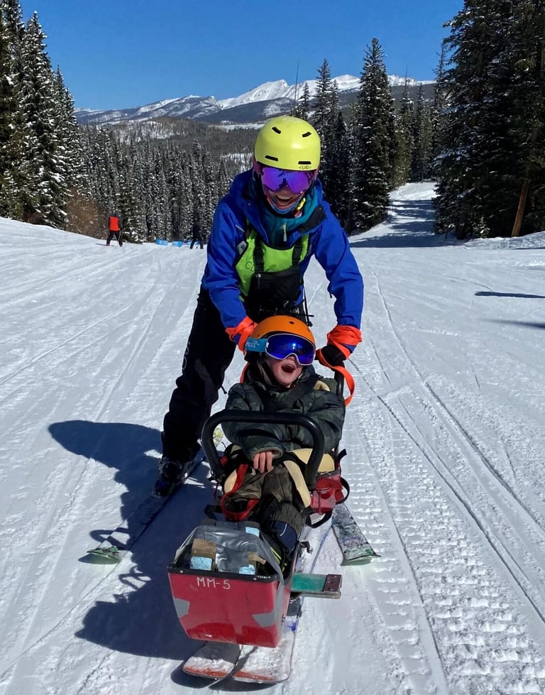 Smiling participant in a sit ski on the mountain, guided by an NSCD instructor