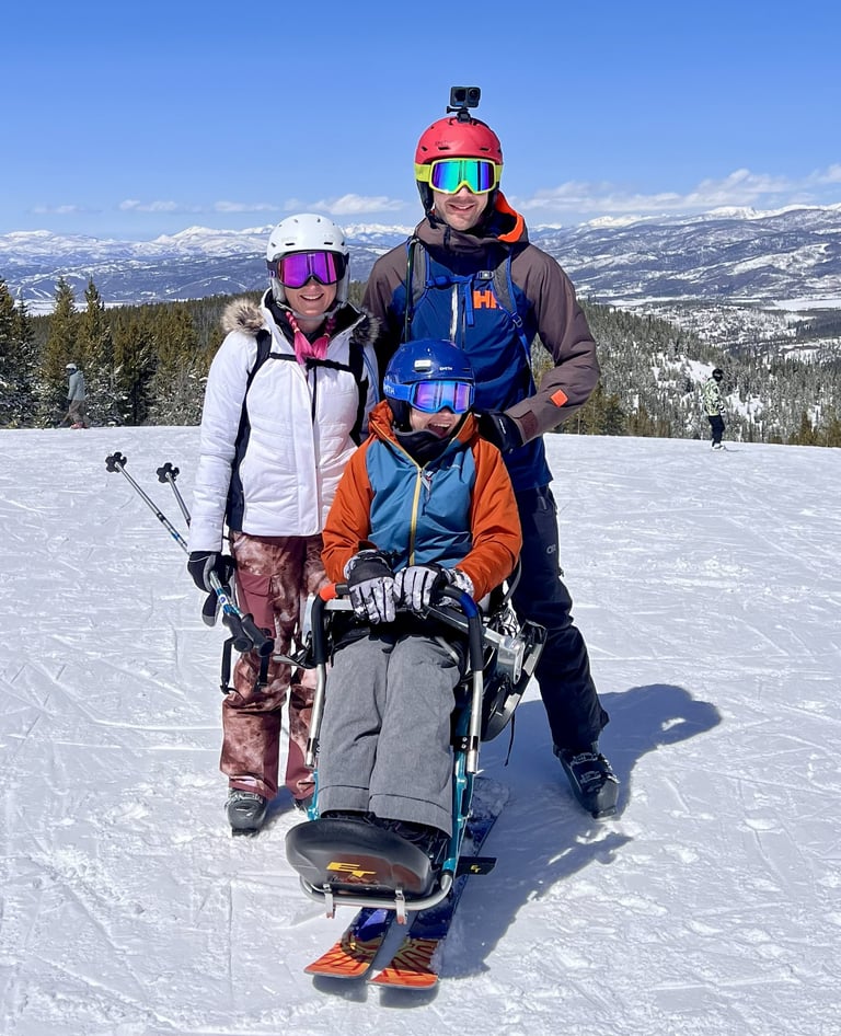 Dorian smiles in his sit ski with his mom, Kelli, and dad beside him during a family ski day at Winter Park Resort.