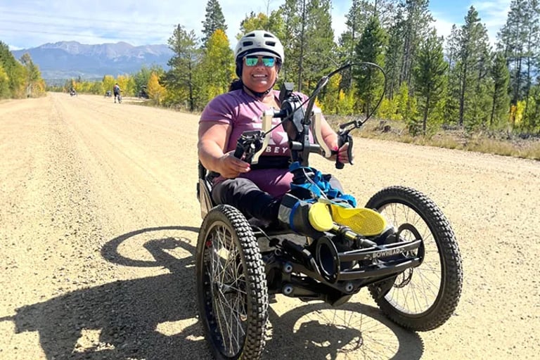 Participant riding an adaptive mountain bike on a dirt road in the mountains.