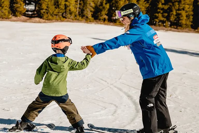 8-year NSCD participant learning to ski by high-fiving volunteers hands as he turns