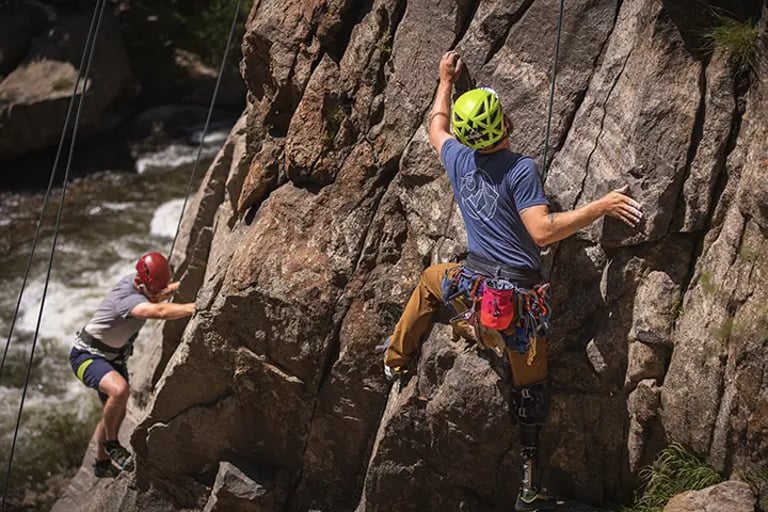 Two participants in rock climbing gear climbing up a steep rock face.