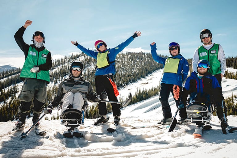 NSCD participants and volunteers on skis and adaptive skis cheering from a ski slope.