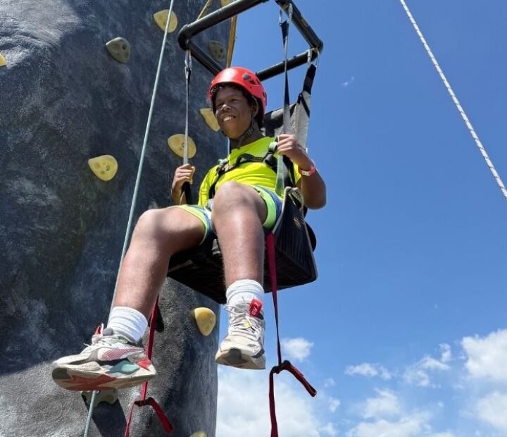 Participant wearing a helmet and adaptive climbing harness while descending from a climbing wall.