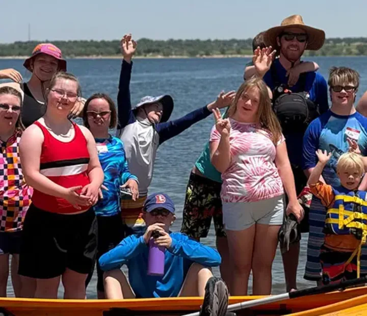 Group of NSCD volunteers and program participants waving from a dock with a kayak floating in front.