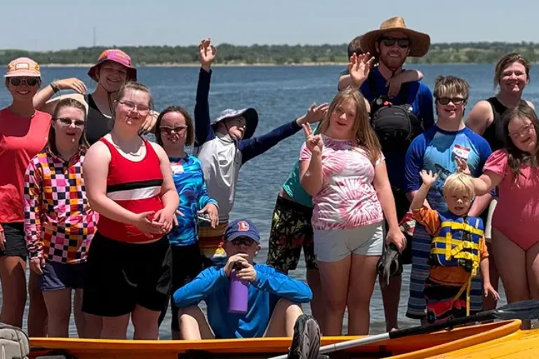Group of NSCD volunteers and program participants waving from a dock with a kayak floating in front.