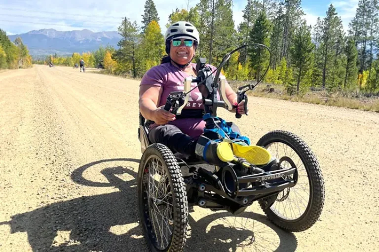 Participant riding an adaptive mountain bike on a dirt road in the mountains.
