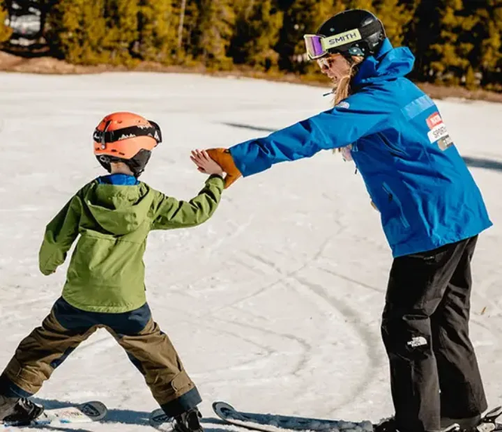 8-year NSCD participant learning to ski by high-fiving volunteers hands as he turns