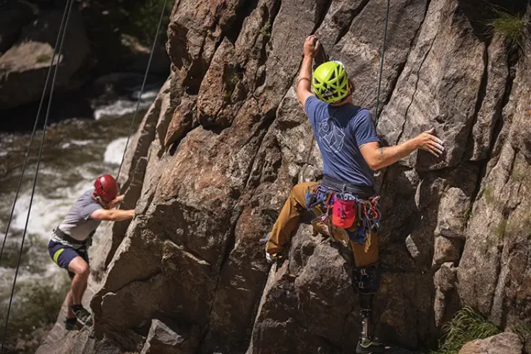 Two participants in rock climbing gear climbing up a steep rock face.