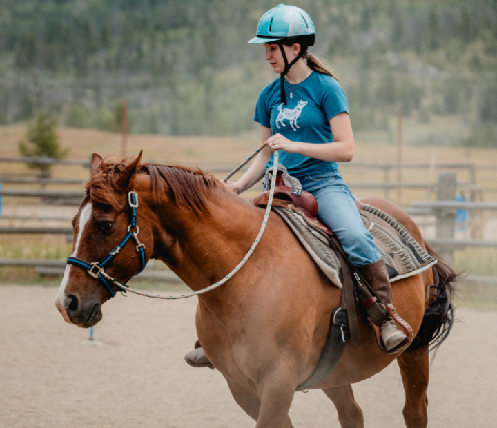 Girl mounted and steering a horse alone while participating in rodeo ready program.