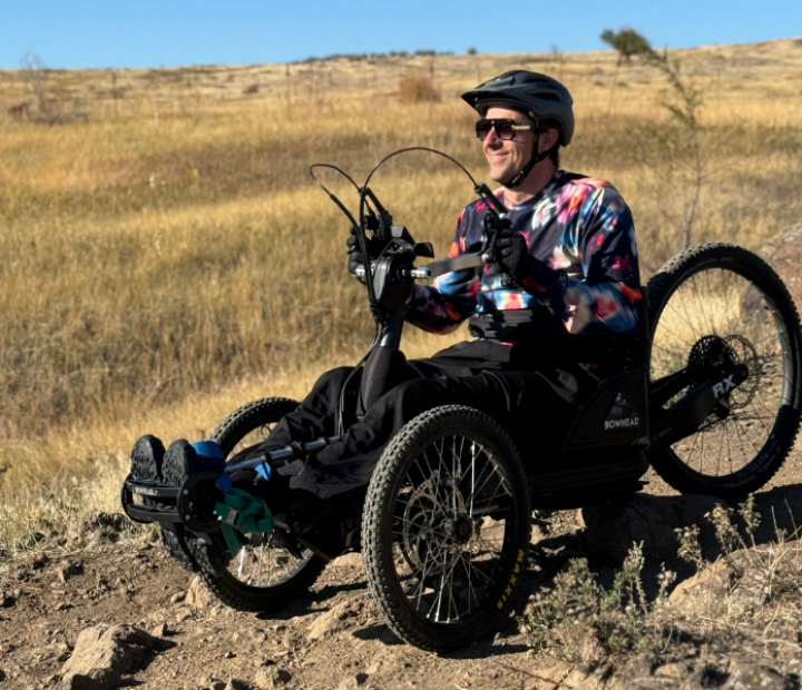 Male participant riding a seating handcycle adaptive mountain bike downhill on a rocky trail.