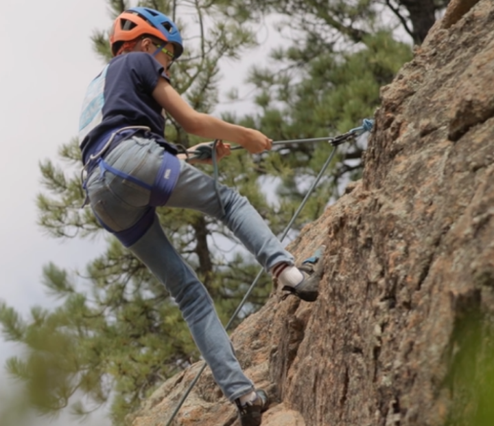 Close up of a young climber at the top of his outdoor climbing route, getting ready to slowly come down from his climb.