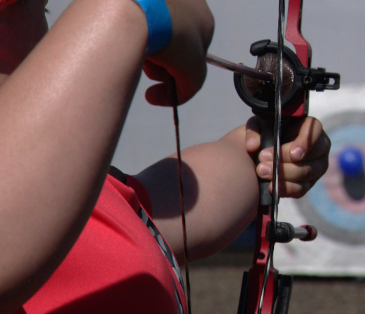 Zoomed in photo of an archer aiming his bow and arrow towards a target with a balloon on it.