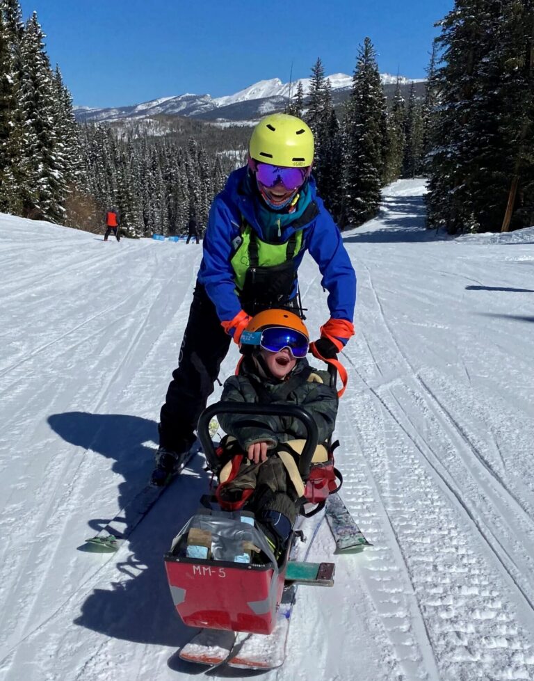 Smiling participant in a sit ski on the mountain, guided by an NSCD instructor