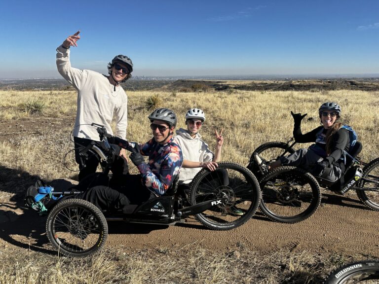 Participants riding adaptive mountain bikes on a trail overlooking the Denver metro area.