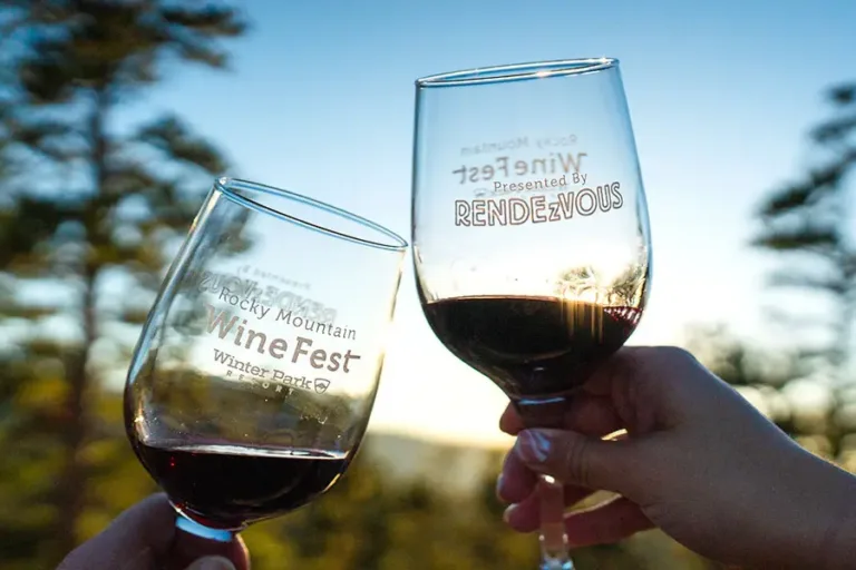 Two wine glasses clinking with the sun behind in a mountain setting.